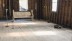 View of the corner of gutted church space with carpeted church bench, two steel stands and various bowls on the floor.