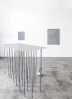 View of thirtyseven legged tall table in front of grey wall hung frames. steel buste on floor